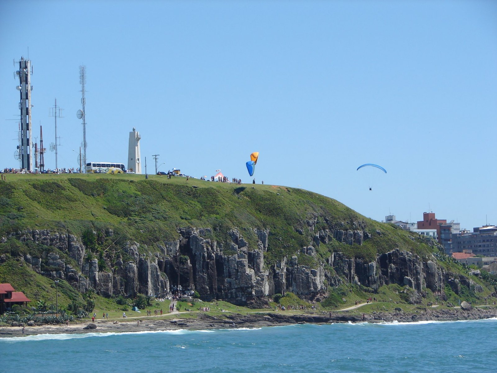 Fotografia do Morro do Farol, em Torres, com o mar e parapentes ao fundo.