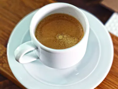 Taza blanca de café sobre un platillo y una mesa de madera. Foto ilustrativa de Shameel Mukkath, Pexels.