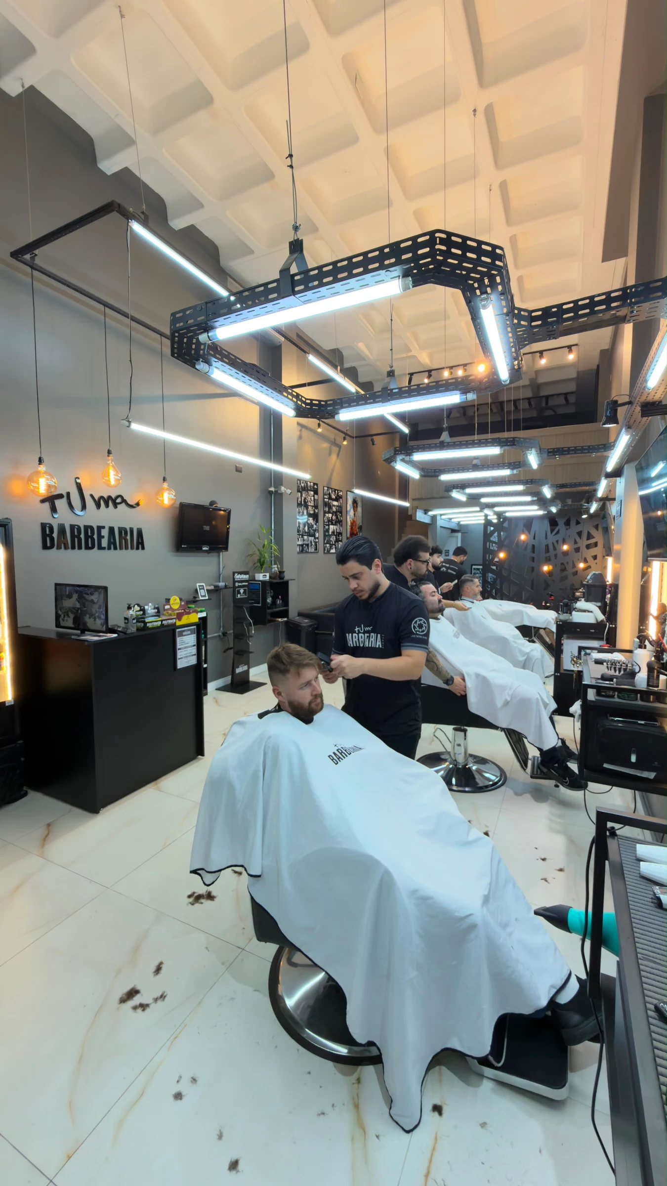 Barbers serving clients in a row of chairs inside Mais Uma Barbearia.
